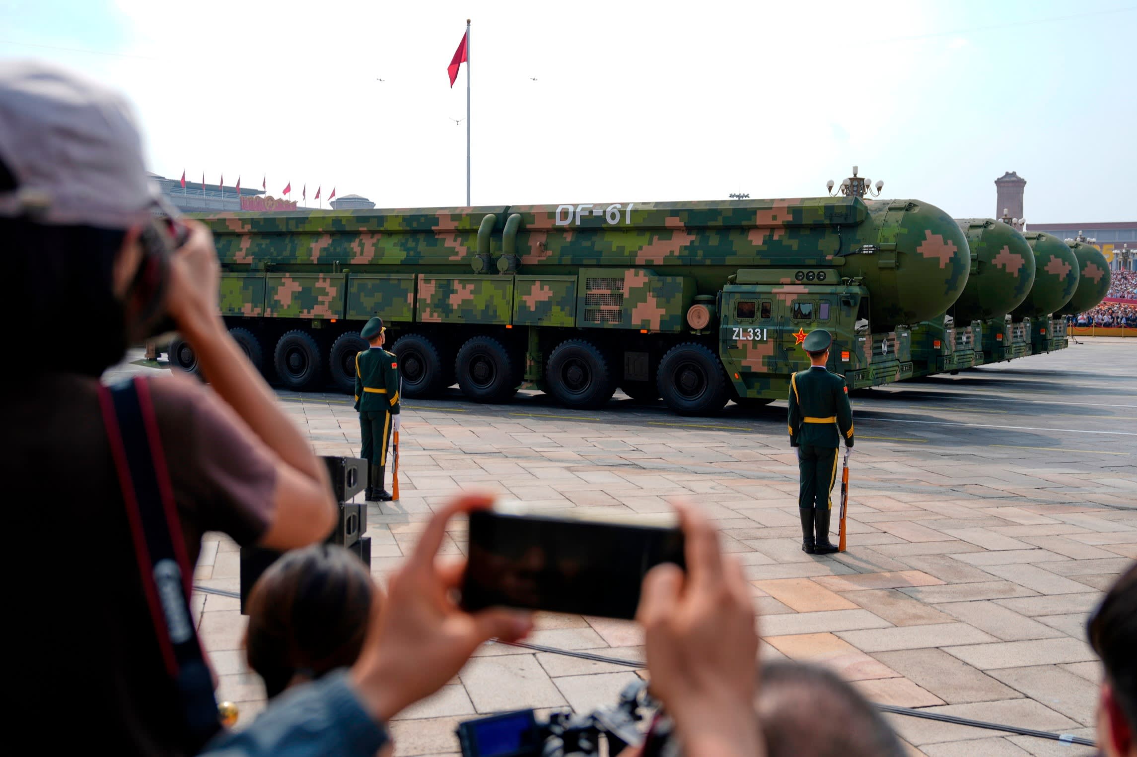 DF-61 missiles on military vehicles pass Tiananmen Gate as uniformed soldiers stand guard and onlookers take photos during a parade.