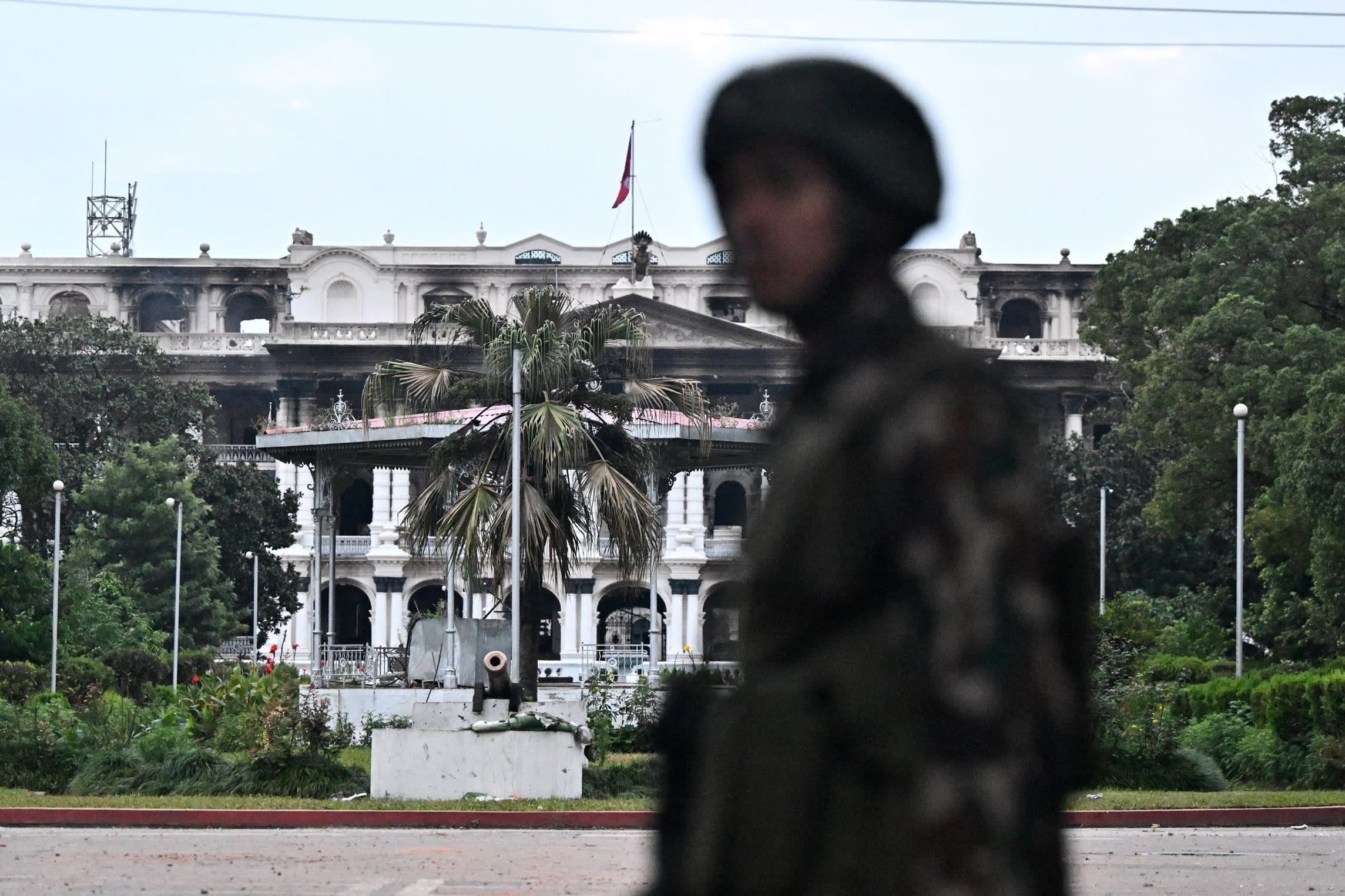 A soldier standing in front of a large burnt-out government administrative building.