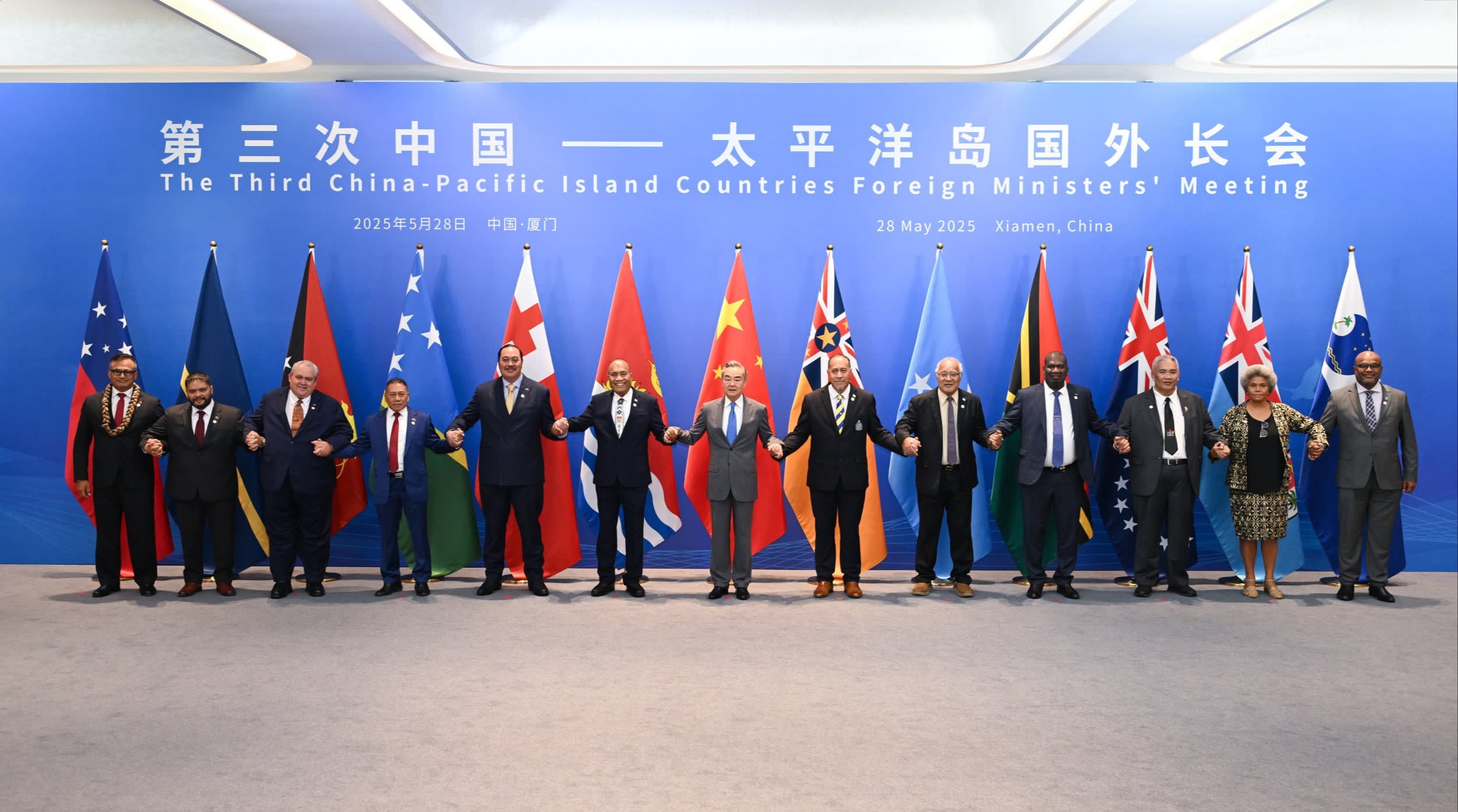 China’s foreign minister Wang Yi holds hands with Pacific island foreign ministers in front of national flags at a meeting in Xiamen in May