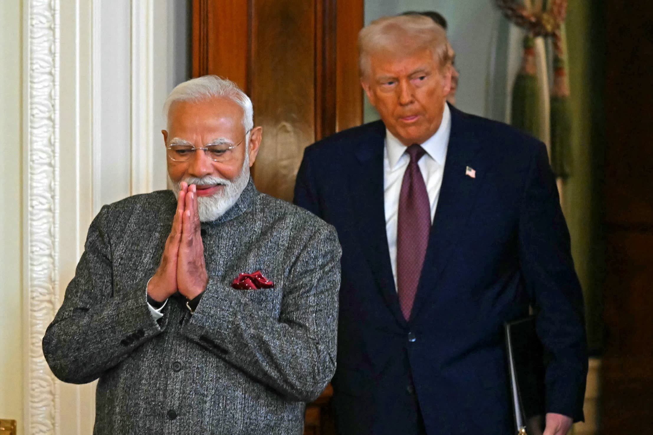 Donald Trump and Narendra Modi entering a room at the White House together, with Modi pressing his hands together in greeting.