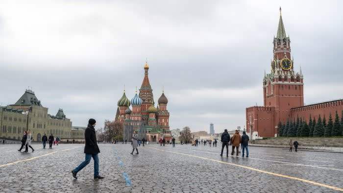 People walk across Red Square in Moscow with St Basil's Cathedral and the Spasskaya Tower of the Kremlin in view.