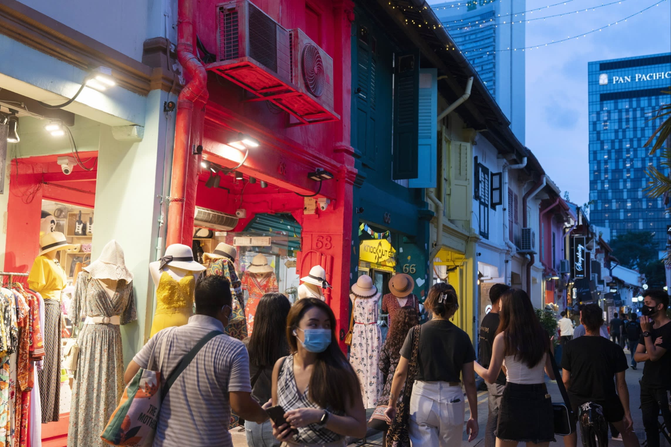 Shoppers walk along a narrow street lined with colorful shophouses and clothing displays at Haji Lane in Singapore.