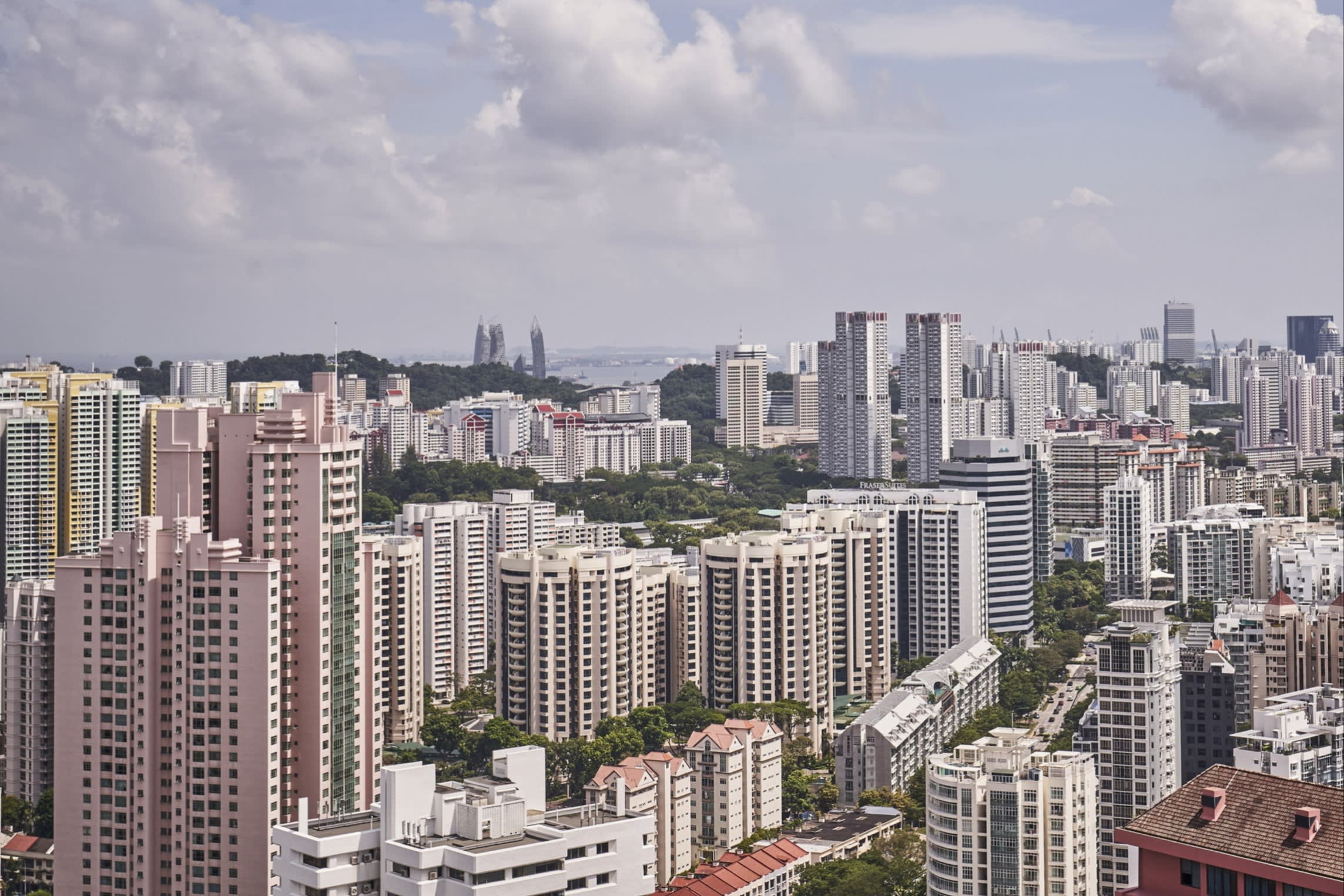 A view of numerous high-rise residential buildings and condominiums in Singapore's River Valley and Orchard area under a partly cloudy sky.