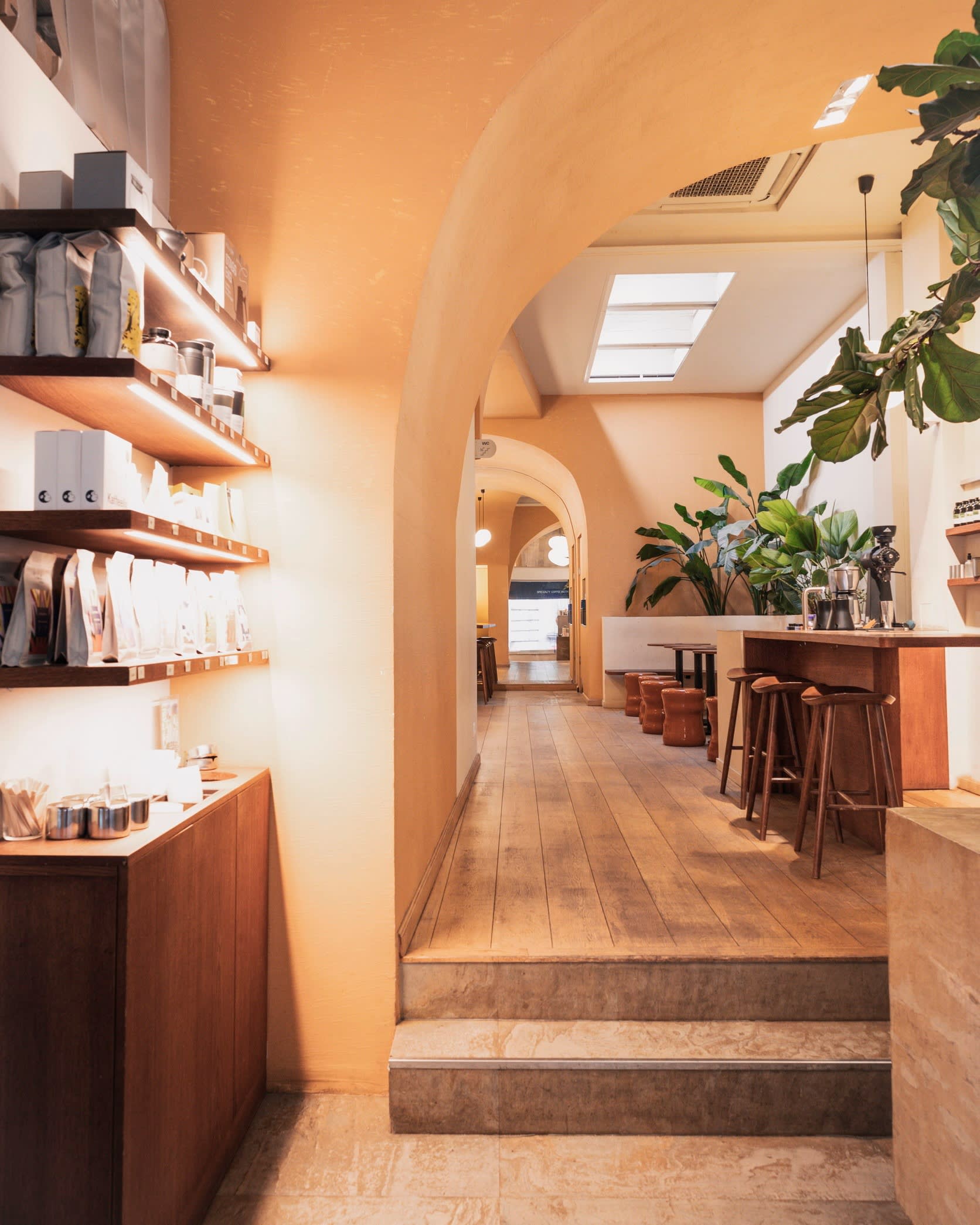 The warmly lit interior of Bouche’s original location, with wooden floors, shelves of packaged goods, bar stools, and large green plants.