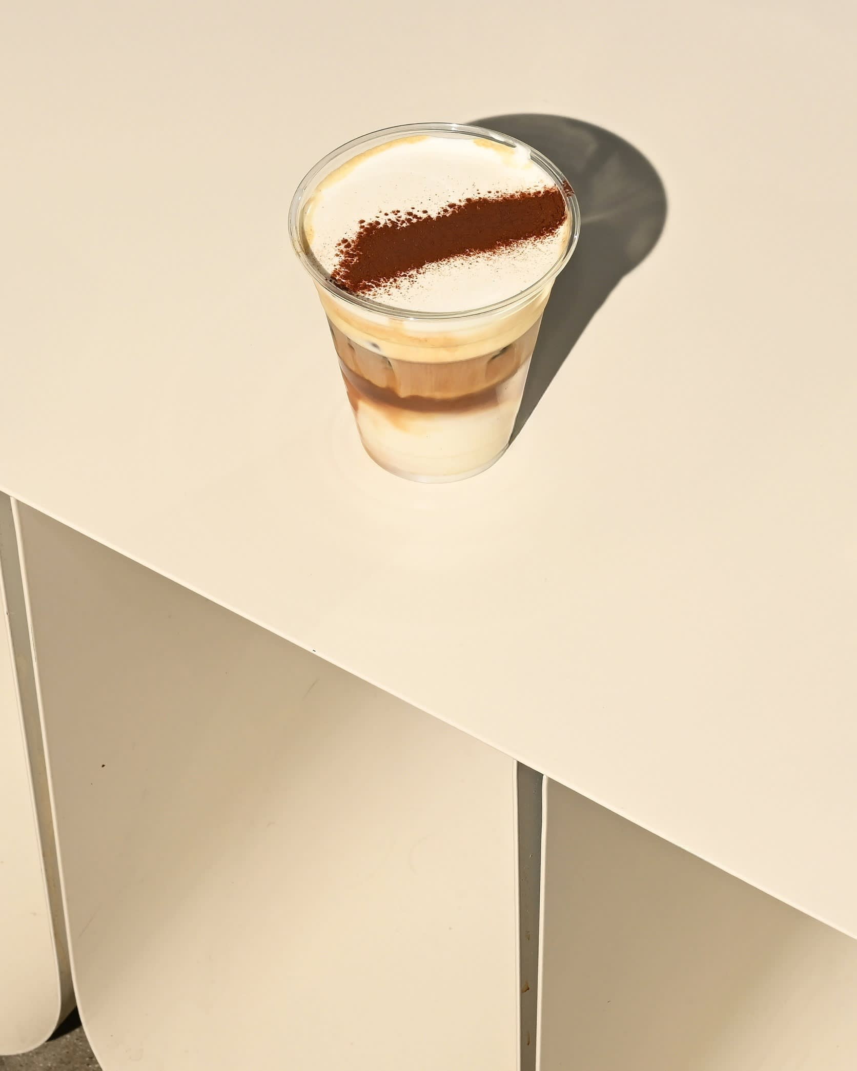 A ‘cream top’ at Stagger in Koreatown, Los Angeles — a cup of iced coffee with a thick cream layer and a diagonal cocoa powder stripe on top, served in a clear plastic cup — standing on a beige counter