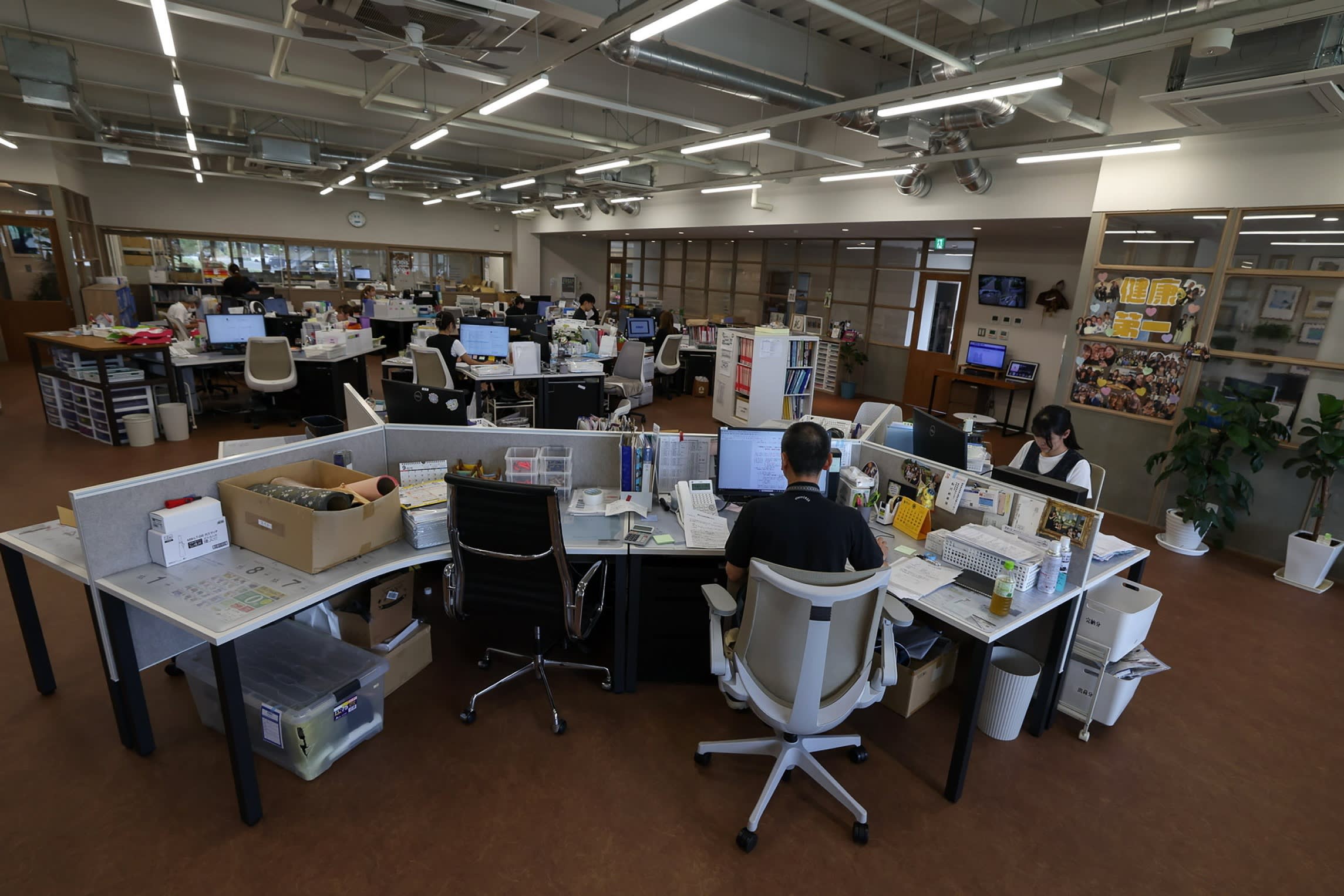 Several employees work at desks with computers and paperwork in a brightly lit open-plan office at Matsukawa Rapyarn.