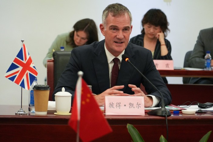 Peter Kyle speaks at a meeting table with UK and Chinese flags, during the UK-China Joint Economic and Trade Commission.