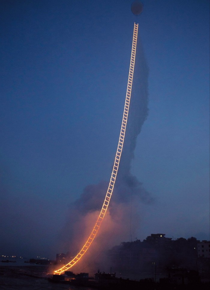 Photograph of what looks like a ladder of fire ascending into the night sky, with a white balloon above it