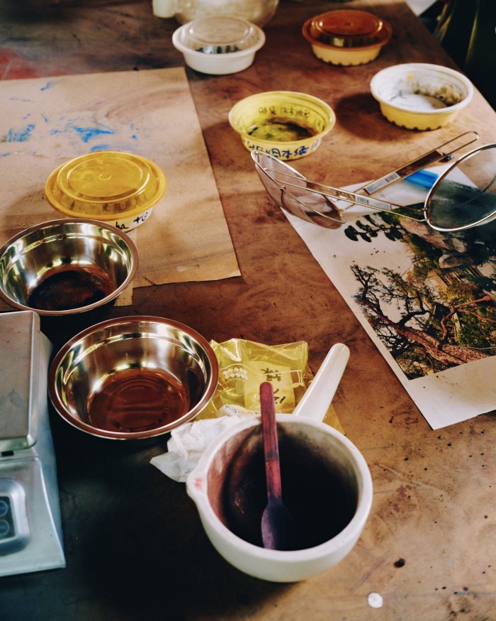 A series of shallow bowls, some containing ink, paint or gunpowder, stand on the table of an art studio, alongside sieves, a set of scales and some pieces of paper