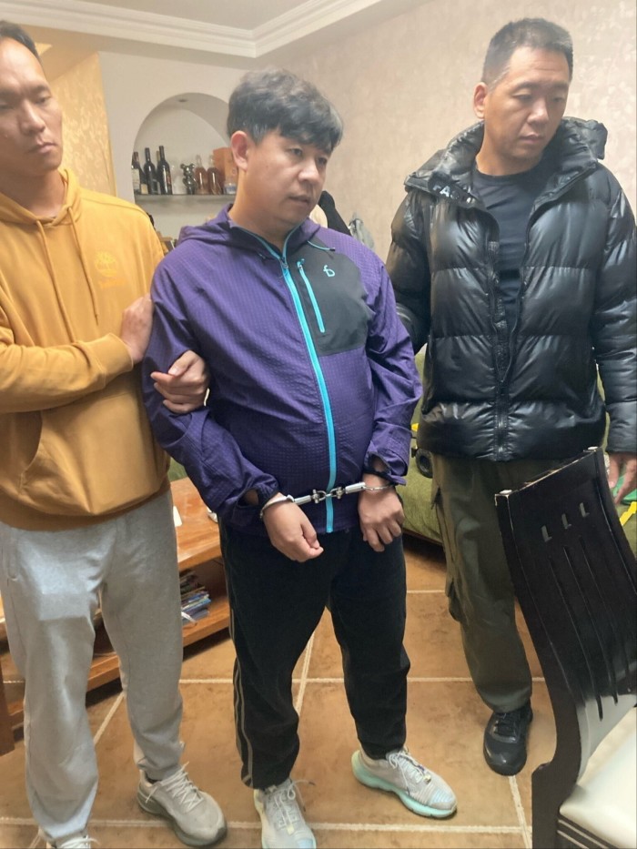 Pastor Sun Cong of Zion Church stands in handcuffs between two men after being detained by police at his home.