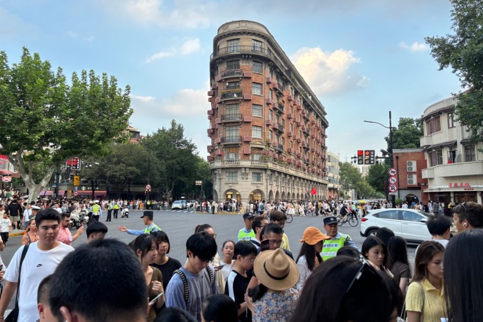 The Wukang Mansion, a historic red-brick building with a rounded corner, stands at a busy intersection crowded with tourists and pedestrians.