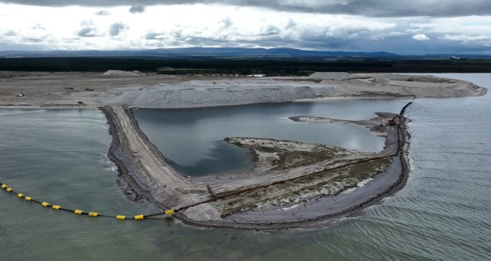 Aerial view of Ardersier Port showing construction work, sand piles, and a partially built causeway extending into the water.