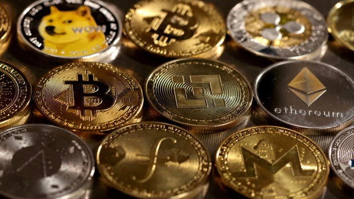 Various physical representations of cryptocurrencies including Dogecoin, Bitcoin, Binance Coin, and Ethereum positioned closely together.
