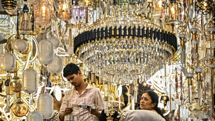 Shoppers examine light fixtures and chandeliers in a brightly lit store filled with crystal and glass lamps