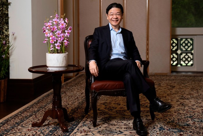 Lawrence Wong sits smiling on a chair in his office, with a potted orchid on a table beside him.
