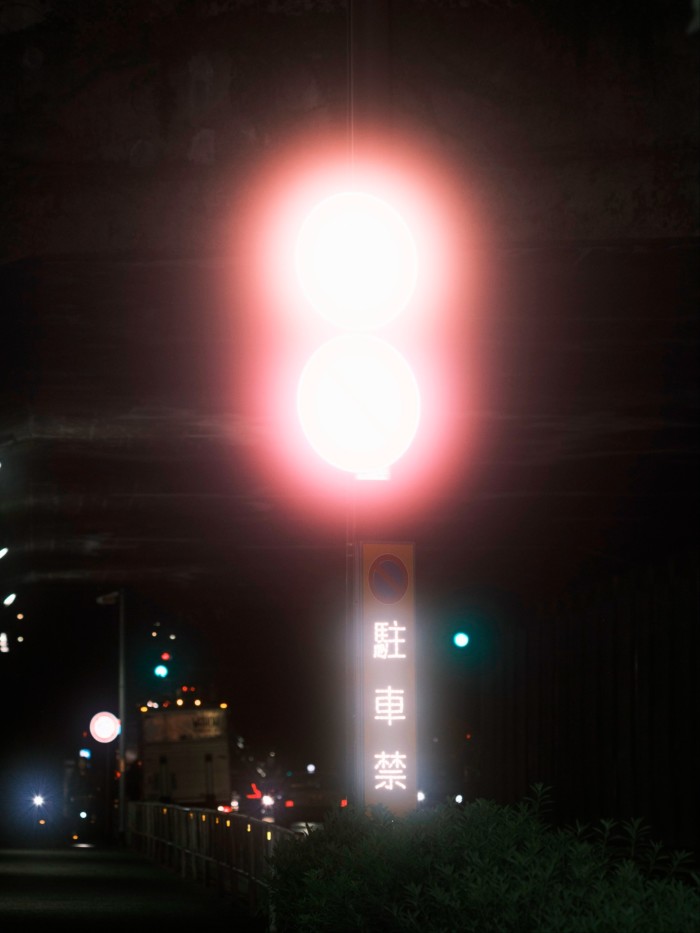 Street signs illuminated by red car lights at night near the Sendagaya Tunnel entrance, with glowing reflections.