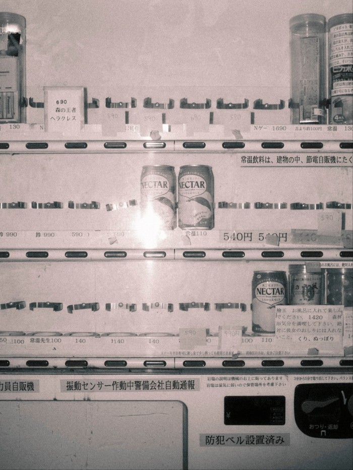 A dimly lit vending machine with mostly empty rows, a few cans labelled "Nectar" and handwritten signs in Japanese.