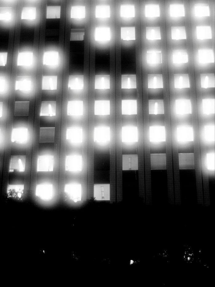 Rows of brightly lit windows on a high-rise building at night, with the lower section in deep shadow, in the Sunshine City complex.