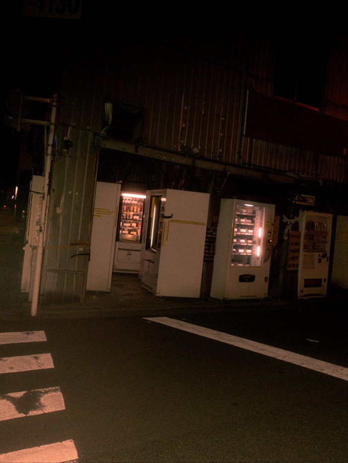 Several vending machines illuminated at night outside a dimly lit building on a quiet street corner in Akihabara.