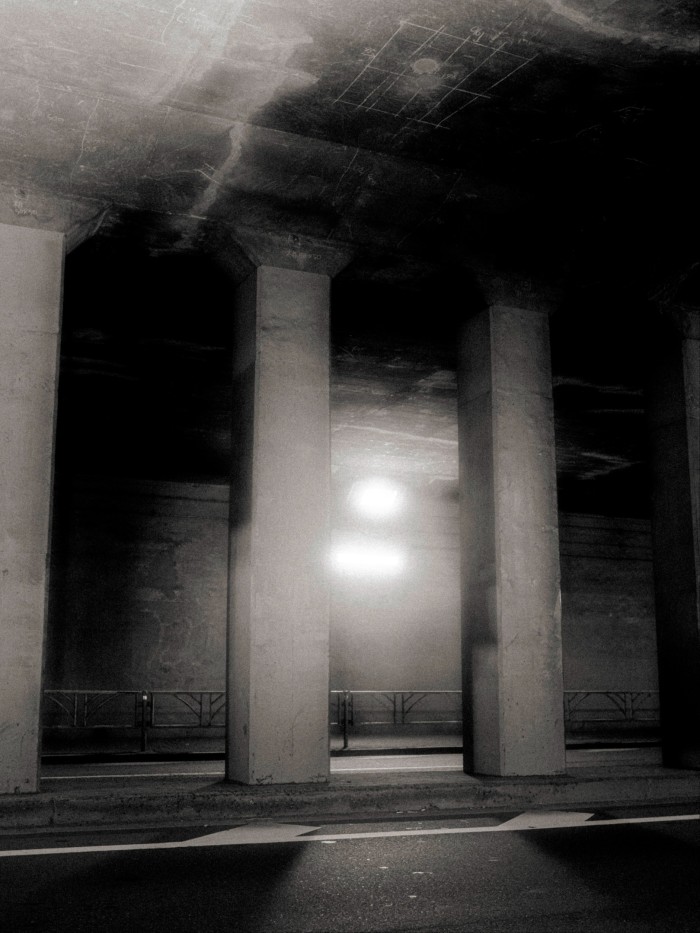 Tall concrete pillars support the ceiling of the Sendagaya Tunnel, illuminated by harsh overhead lights and casting deep shadows.