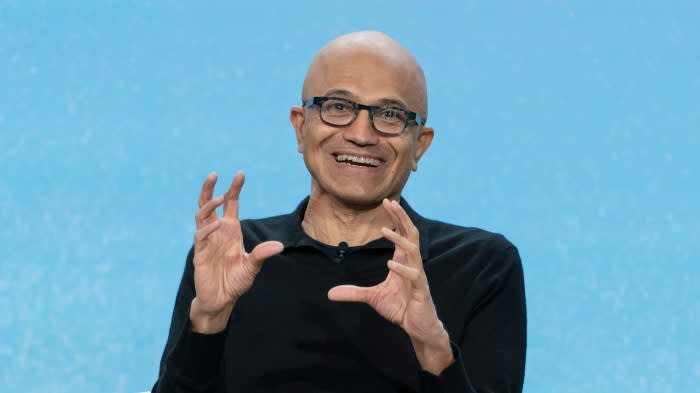 Satya Nadella gestures with both hands while speaking, smiling during the Microsoft 50th anniversary event.