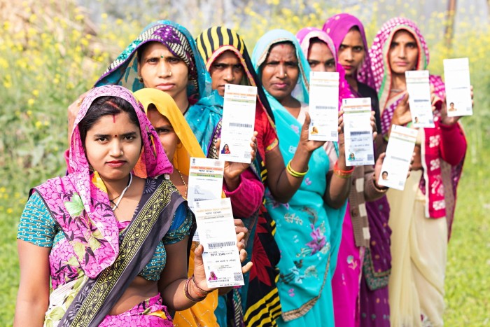 A group of rural women standing in a field, each holding up their Aadhaar government identity card.