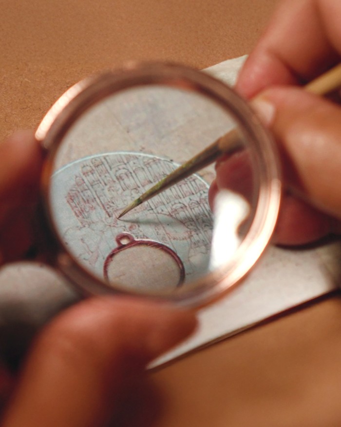 Close-up of a person painting fine details on a watch dial using a magnifying lens.