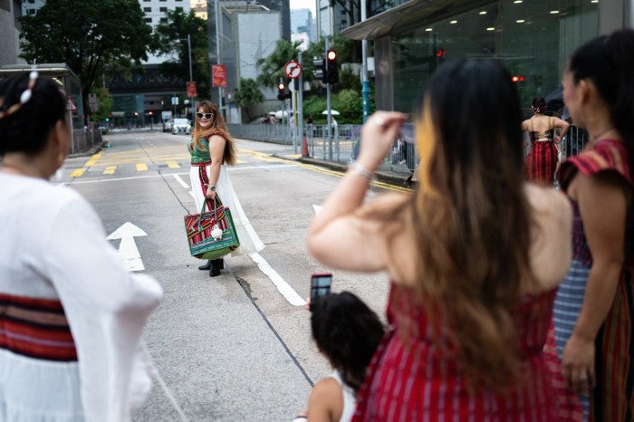 A group of women, some in traditional dress, watch as one woman poses for a photo on a city street in Central, Hong Kong.
