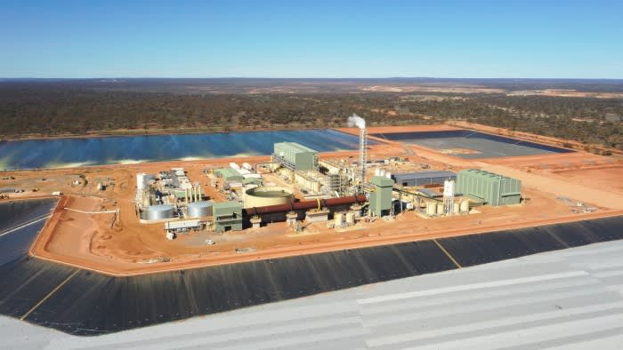 Aerial view of the Lynas Rare Earths processing plant with industrial buildings, storage tanks, and a smokestack surrounded by red soil and water ponds.