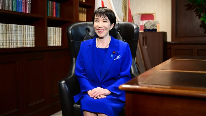 Sanae Takaichi sits smiling in a blue suit in the party leader's office after winning the LDP leadership election.