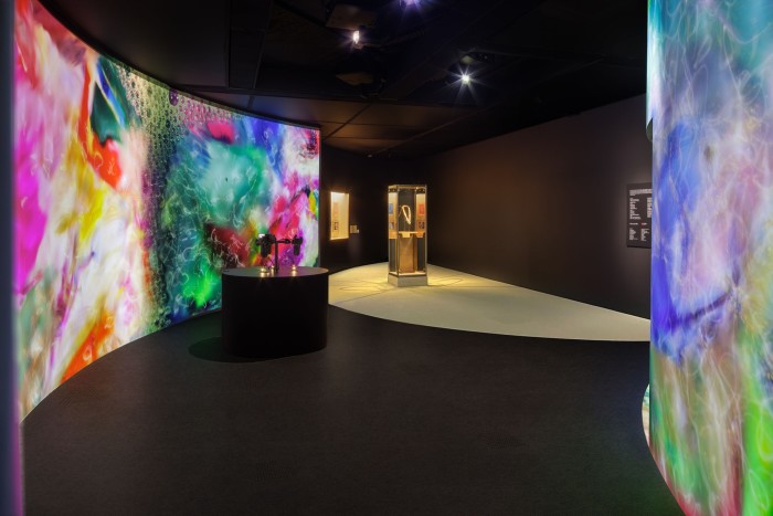 A gallery interior with curved metallic walls and vitrines showing jewels.