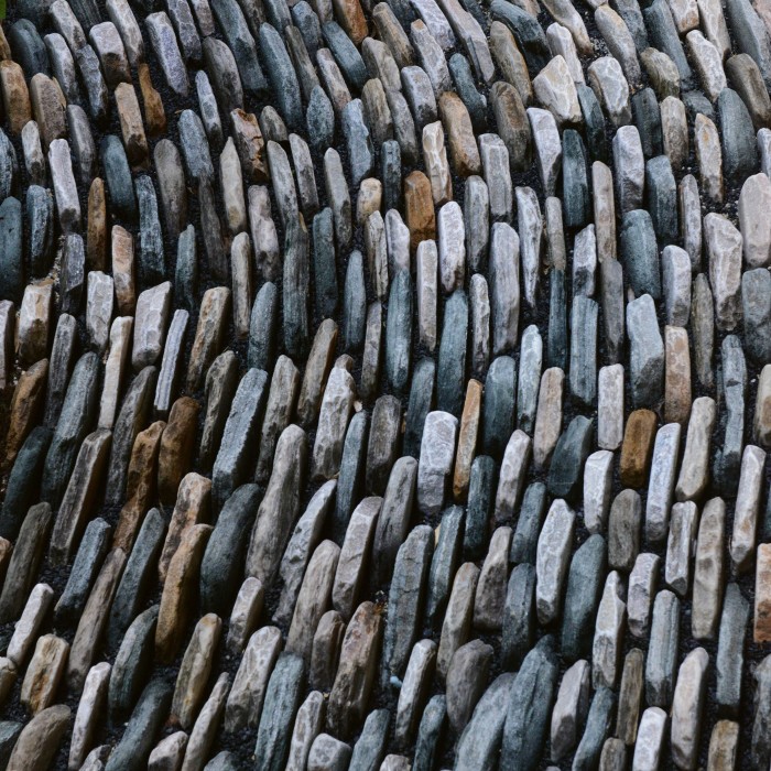 Close-up of smooth, upright stones arranged in a wavelike pattern, creating a textured surface of grey and brown tones.
