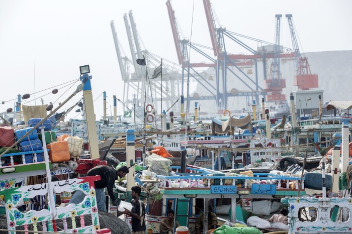 Closely packed fishing boats with large cranes in the background at Gwadar