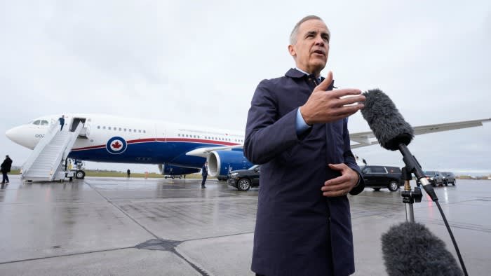 Mark Carney speaks to reporters in front of microphones in front of a Canadian government plane.