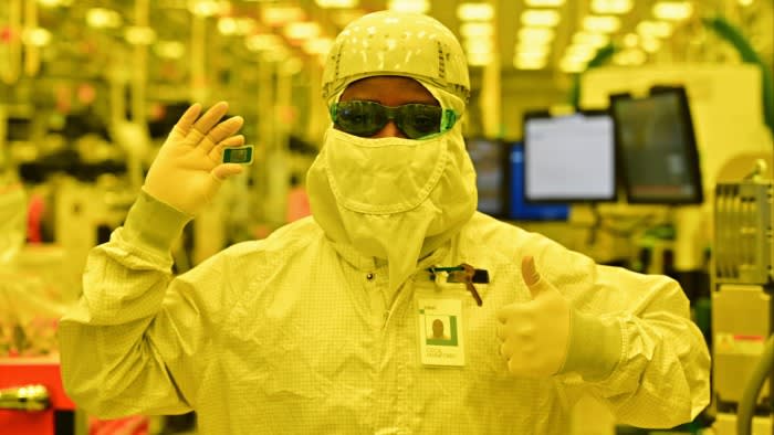 Cecil Manford in a cleanroom suit holds up a computer chip with one hand and gives a thumbs up at an Intel facility.