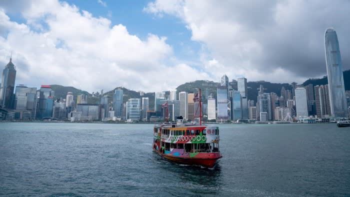 A Star Ferry painted with colourful patterns crosses Victoria Harbour with the Hong Kong skyline and skyscrapers in the background.