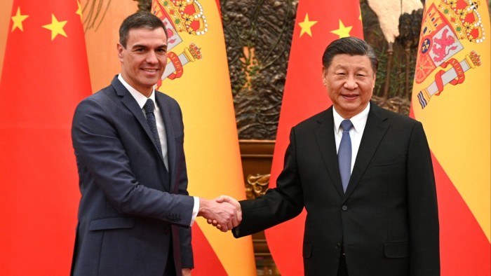 Xi Jinping and Pedro Sánchez shake hands, standing in front of Chinese and Spanish flags. Both are smiling.