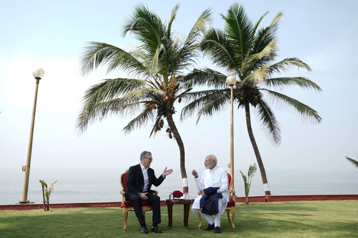 Keir Starmer and Narendra Modi seated outdoors in discussion, with palm trees and the sea in the background.