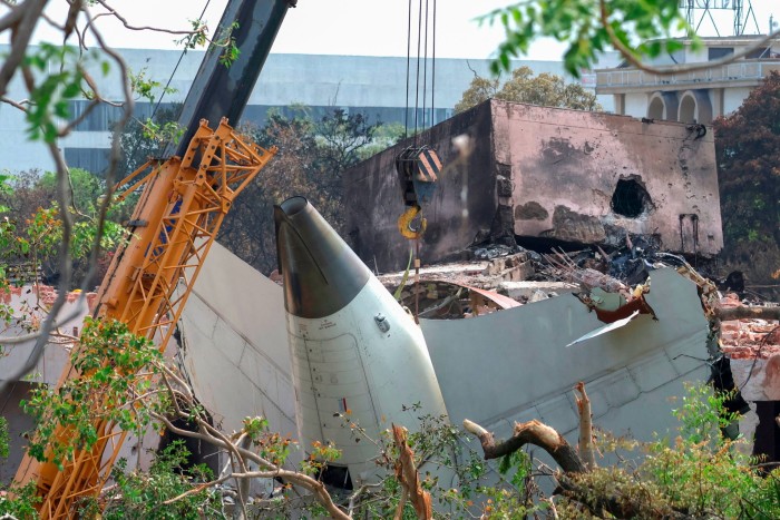 A crane lifts the damaged nose section of an Air India Boeing 787-8 Dreamliner amid debris and a partially destroyed building.