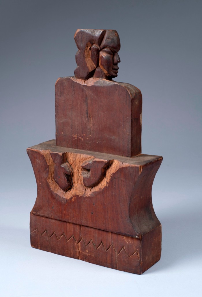A carved wooden sculpture featuring a stylised seated figure with a geometric torso and a defined head in profile