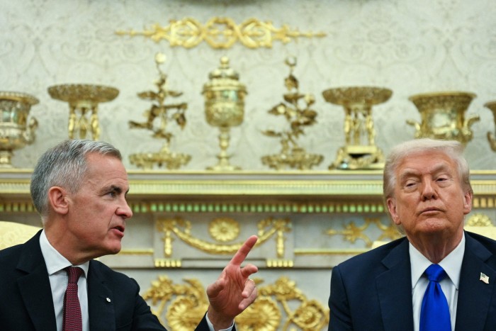 Mark Carney gestures while speaking to Donald Trump during a meeting, both seated in front of ornate gold decorations.