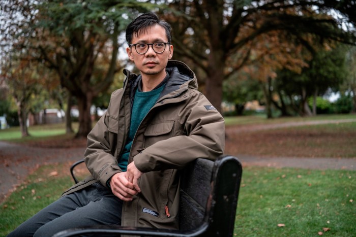 Richard Choi sits on a park bench with autumn trees in the background.
