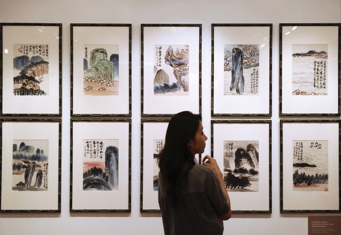 A woman examines Qi Baishi’s ‘Landscapes’ paintings displayed in two rows of framed artwork at an auction preview.