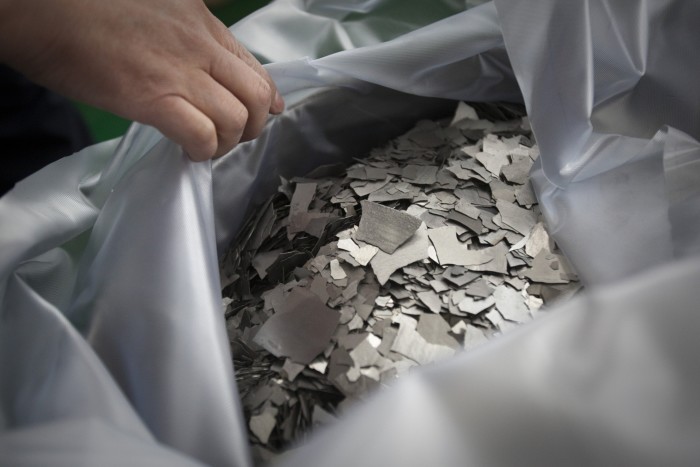 Neodymium metal flakes in a large bag are displayed at a factory, with a hand pulling back the plastic covering.