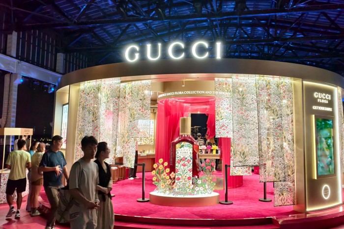 A Gucci pop-up store with floral-themed decor and a large display perfume bottle, with people walking past at night.