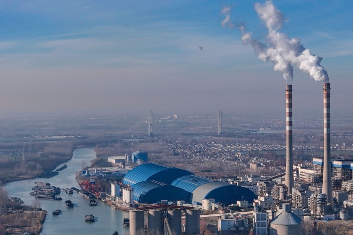 Huaneng Huaiyin Power Plant with large blue-roofed buildings and two smokestacks emitting white smoke near a river with barges.