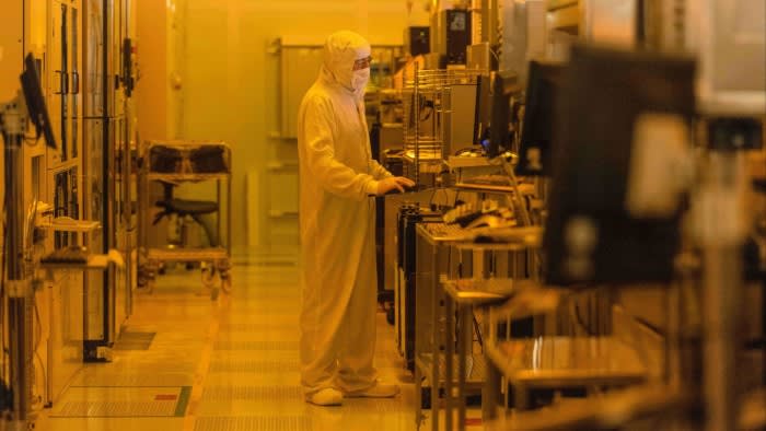 A worker in a full cleanroom suit operates equipment inside the Newport Wafer Fab semiconductor manufacturing facility.