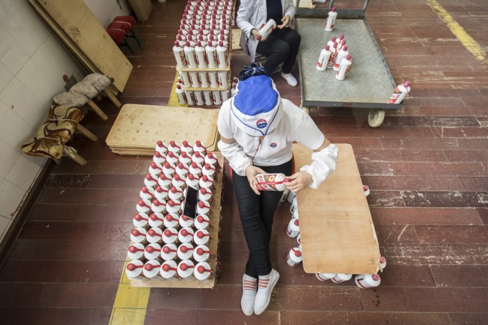 An employee in a white uniform and blue cap arranges rows of Moutai baijiu bottles at a factory workstation