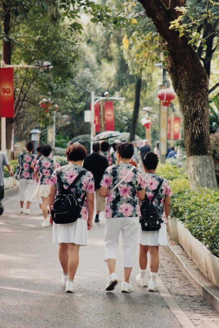 A group of women in matching floral tops and white shorts, seen from behind as they walk through a park.
