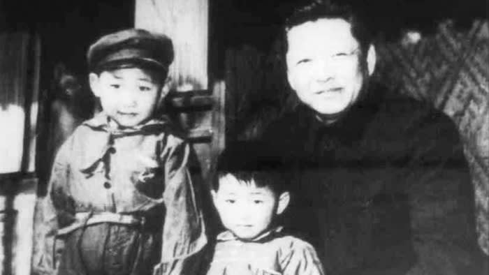 A faded black-and-white photograph of a man in a black Communist-style suit crouching next to two young boys
